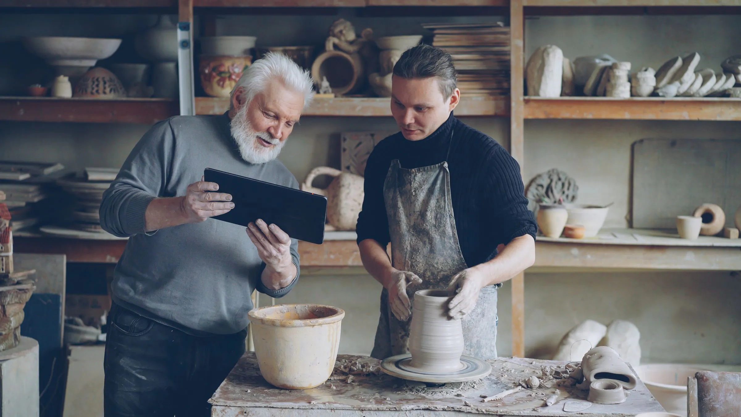 A master potter reviewing a student’s work at the wheel